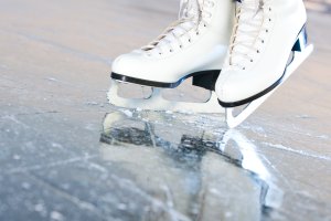 Gros plan d'une paire de patins artistiques blancs sur la glace, montrant les lames des patins et la surface rayée de la glace.