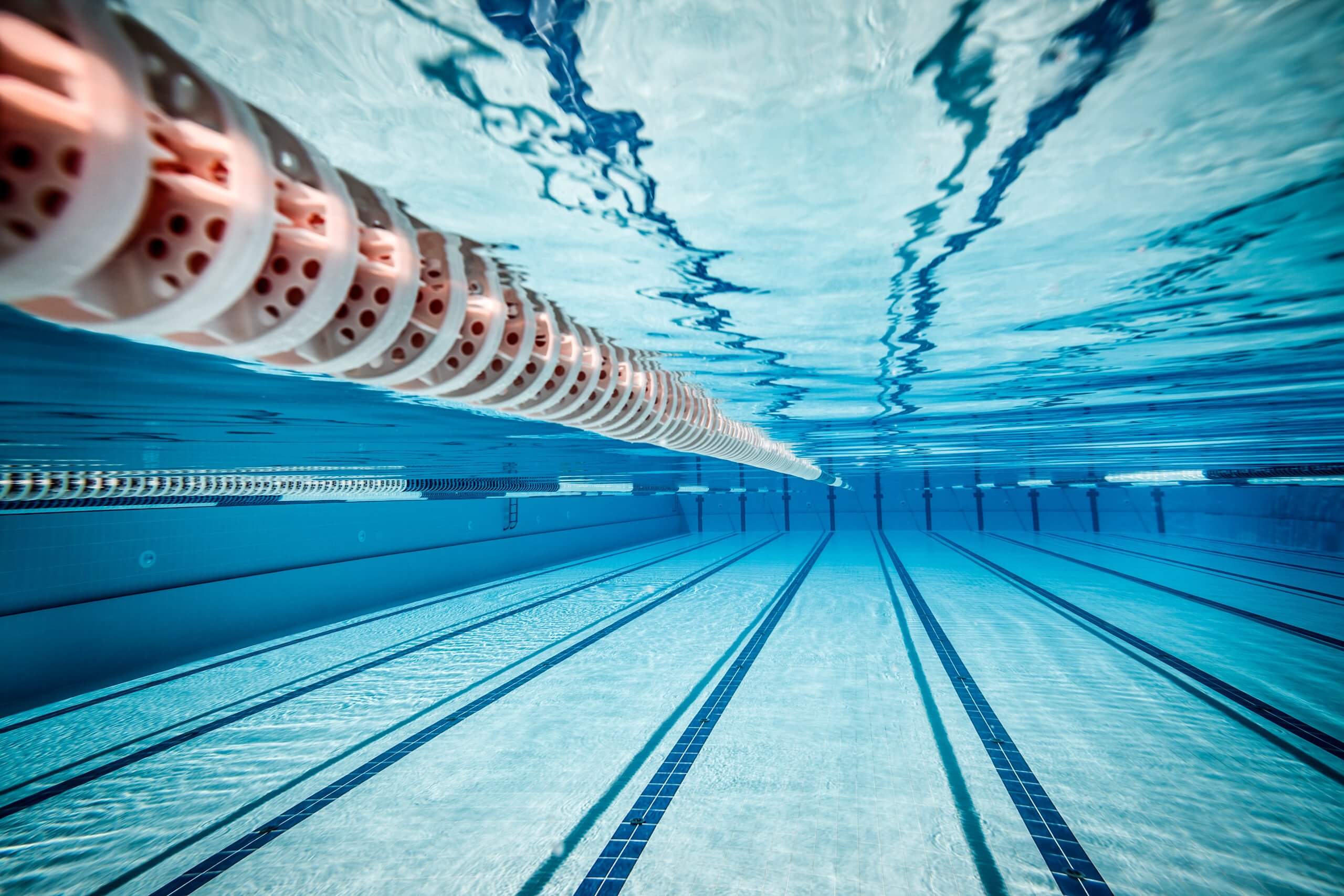 Unterwasseransicht eines leeren Schwimmbeckens mit sichtbaren Bahnen und blau gefliestem Boden.