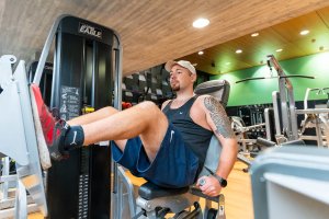Un homme en tenue de sport utilise une machine à presser les jambes dans un gymnase, poussant la plate-forme avec ses pieds tout en étant assis.