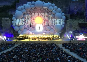 Une scène de concert en plein air présente une grande toile de fond en forme de ballon sur laquelle est projetée 