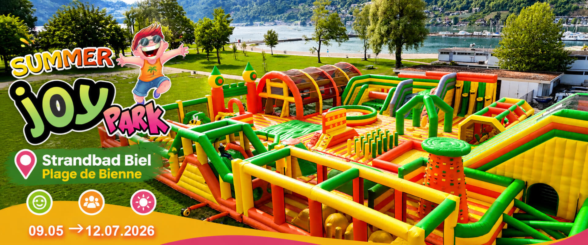Un grand parcours d'obstacles gonflable aux couleurs vives est installé sur une zone herbeuse près d'un lac, avec les détails de l'événement Summer Joy Park au Strandbad Biel.
