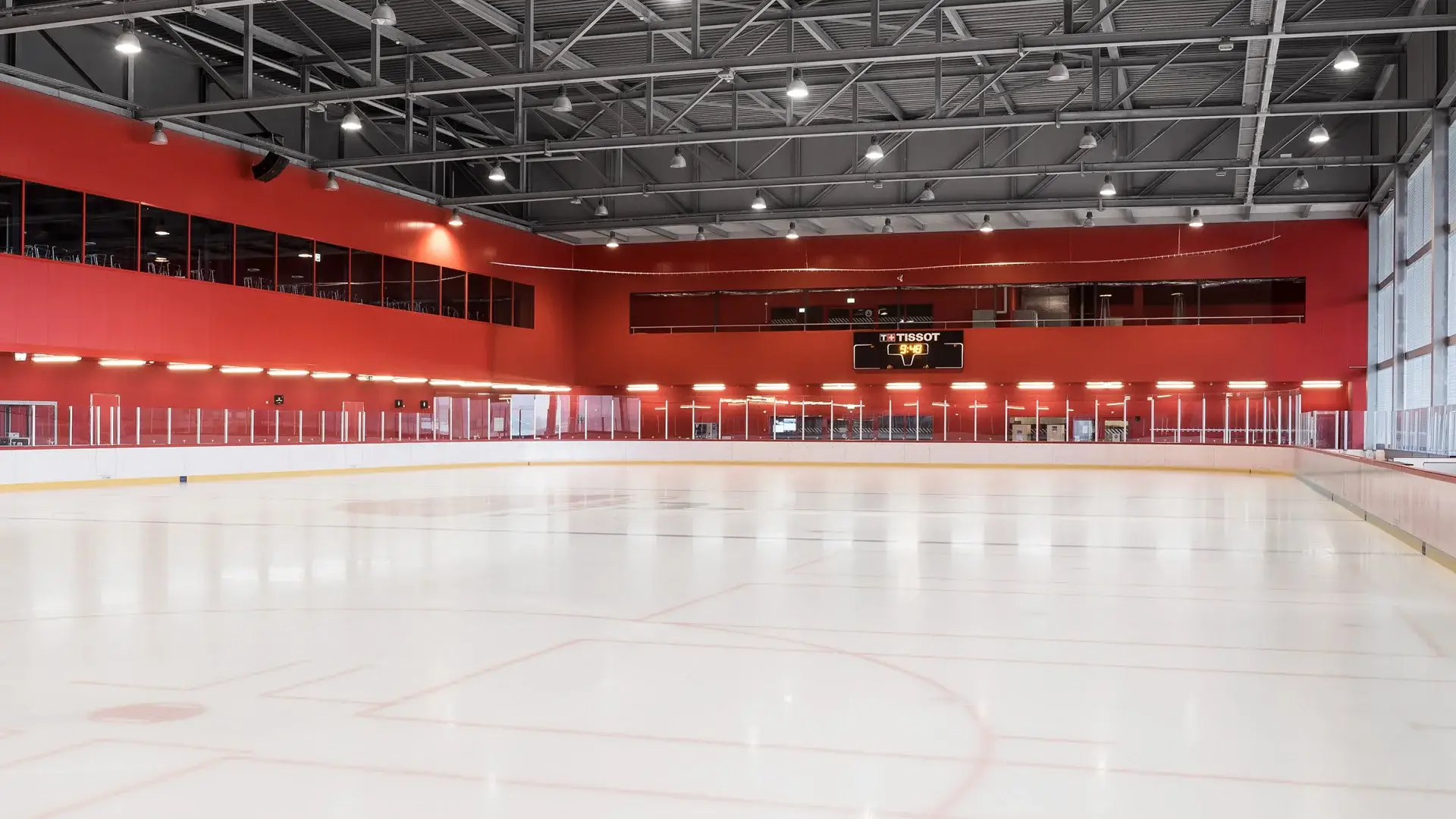 Eine leere Eishockeyhalle mit roten Wänden und einer digitalen Anzeigetafel.